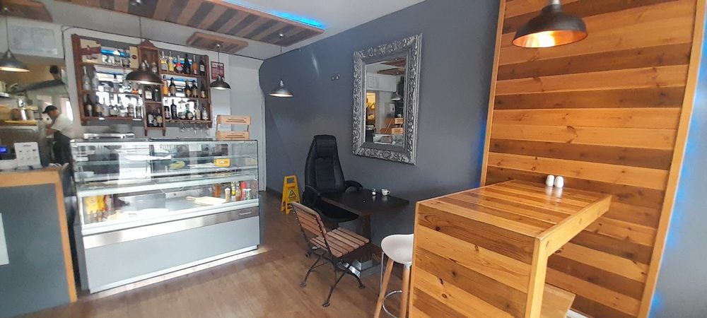 The seating area at Café Do Brazuca, with the glass cake counter, mirror and timber-clad wall above wooden tables