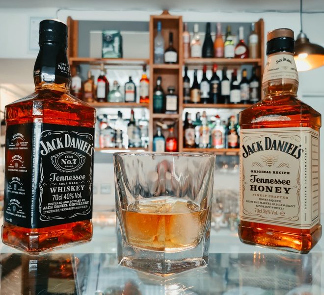 Bottles and a tumbler on the bar in front of the backbar spirits shelf, cropped away from the burned-in wording