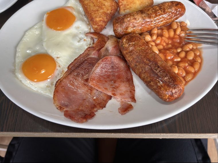 A close full English plate with fried eggs, bacon, sausages and beans